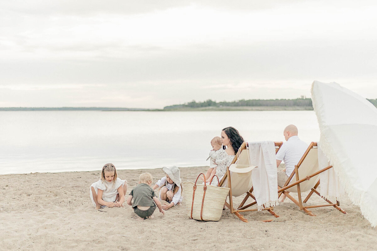 Family of six sitting and lounging together under a white umbrella during a milestone photo session by a Kansas City lake. 