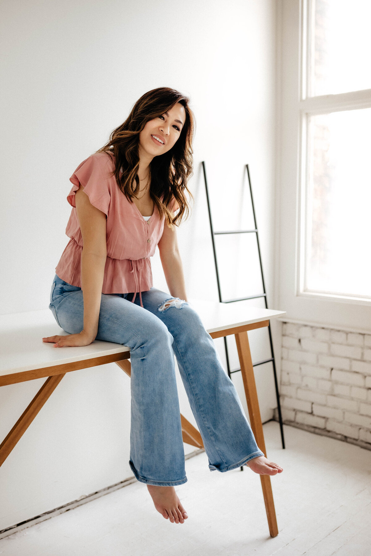 woman in pink shirt sitting on desk smiling. 