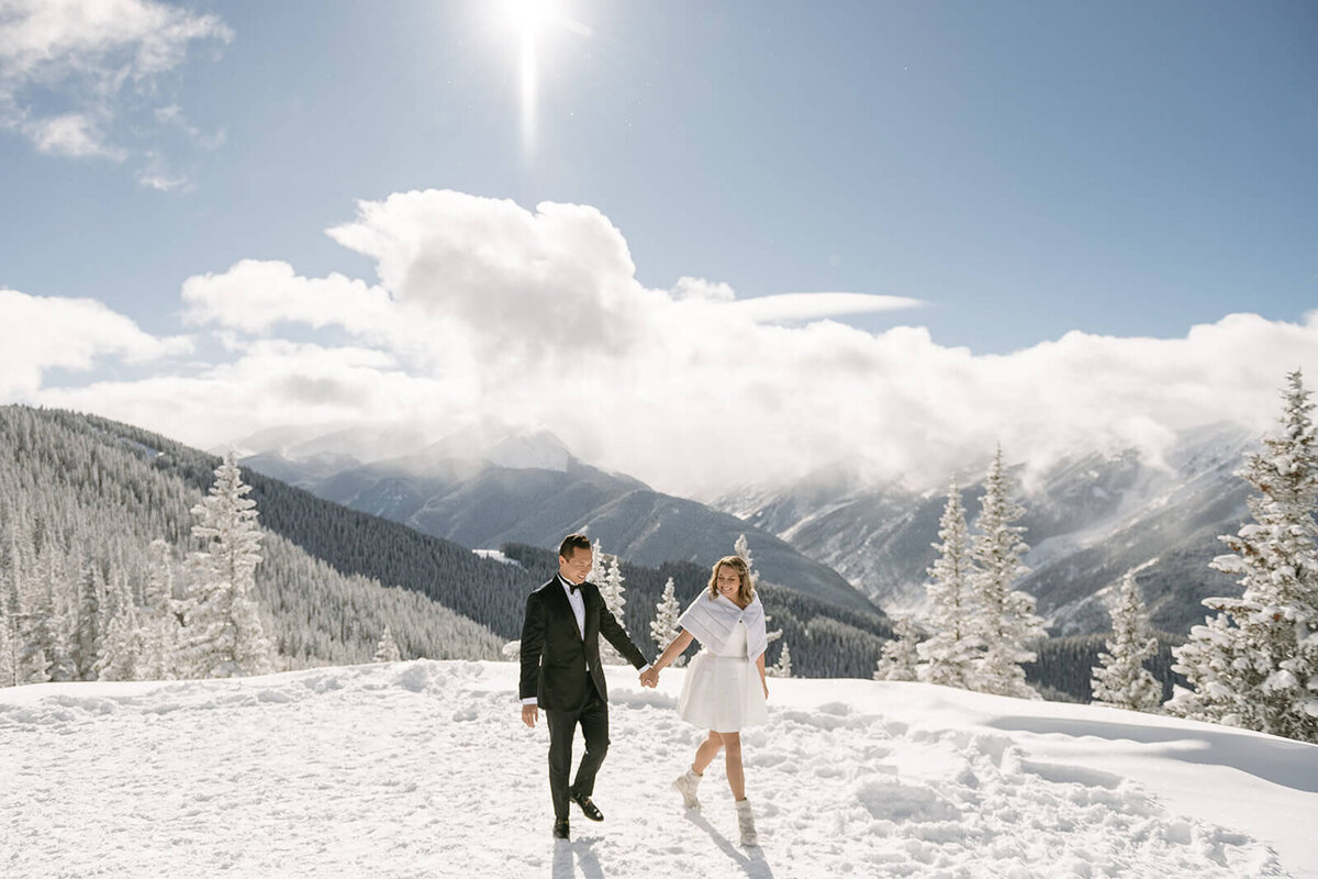 On the top of snowy Aspen Mountain, a bride and groom walk hand in hand.