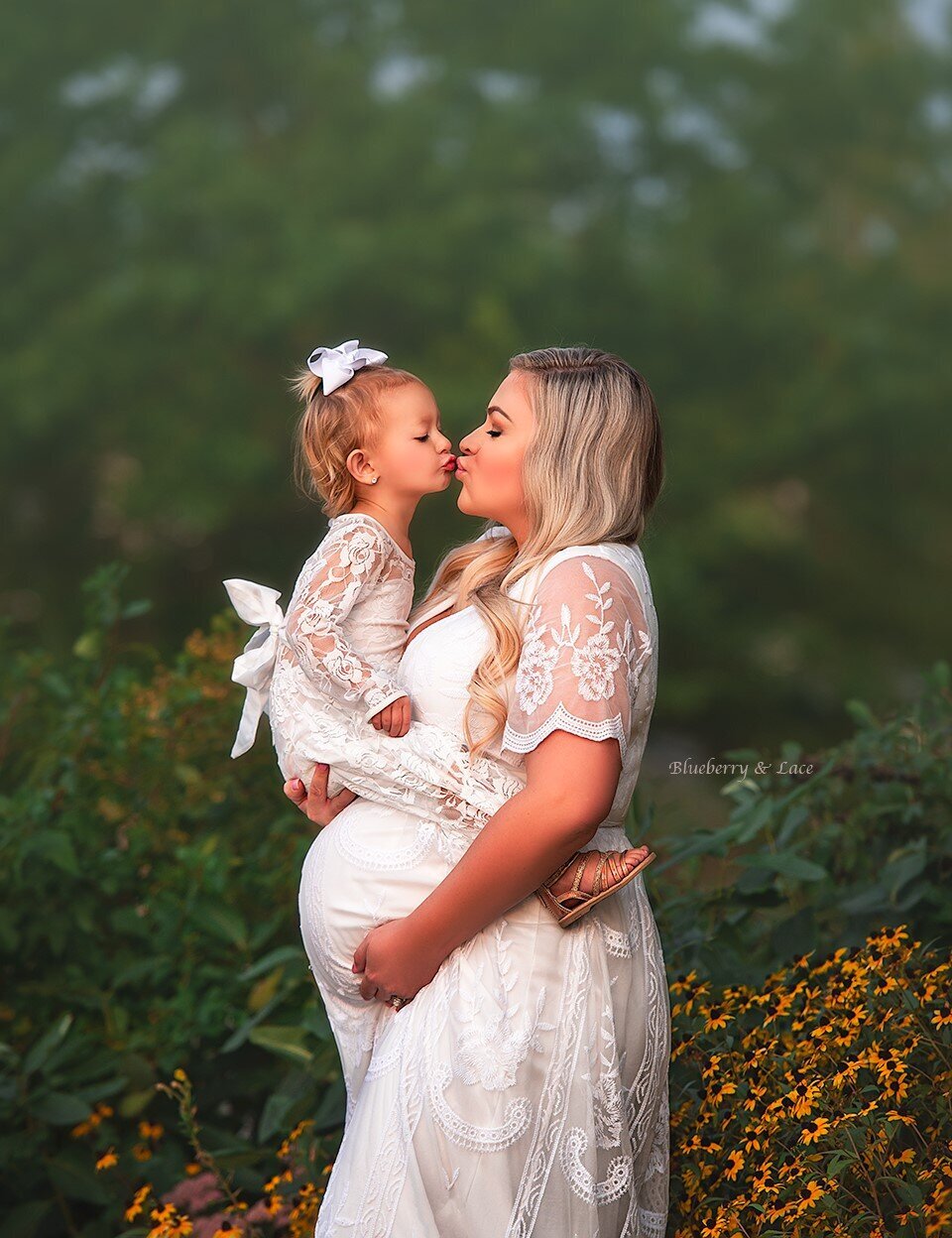 mother and daughter kissing while mother is pregnant holding onto her bump outdoors fine art