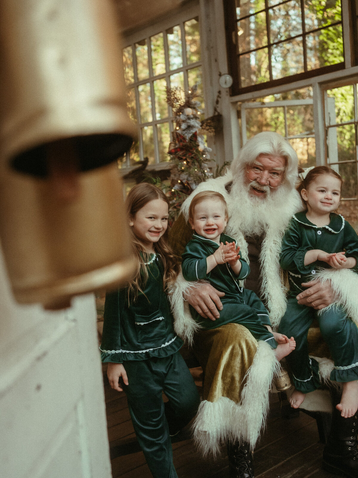 Three siblings in matching silk green pajamas sitting in Santa's lap at Das Hinterhaus Studio.