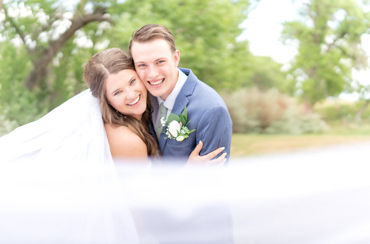 Bride and groom leaning in together towards the camera smiling on their wedding day with the bride's veil framing the picture