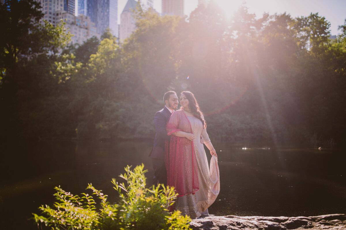 A couple sharing a moment by the central park pond by the gapstow bridge in indian clothing during their engagement shoot