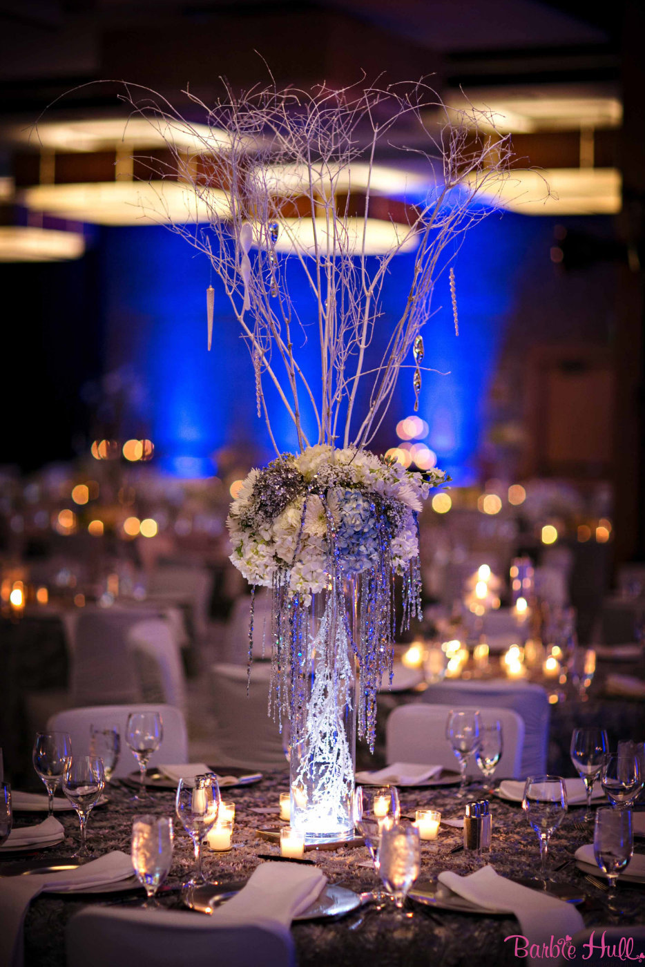 tall winter party centerpiece of white and bklue hydrangea, with tall sparkle branches, on silver linen