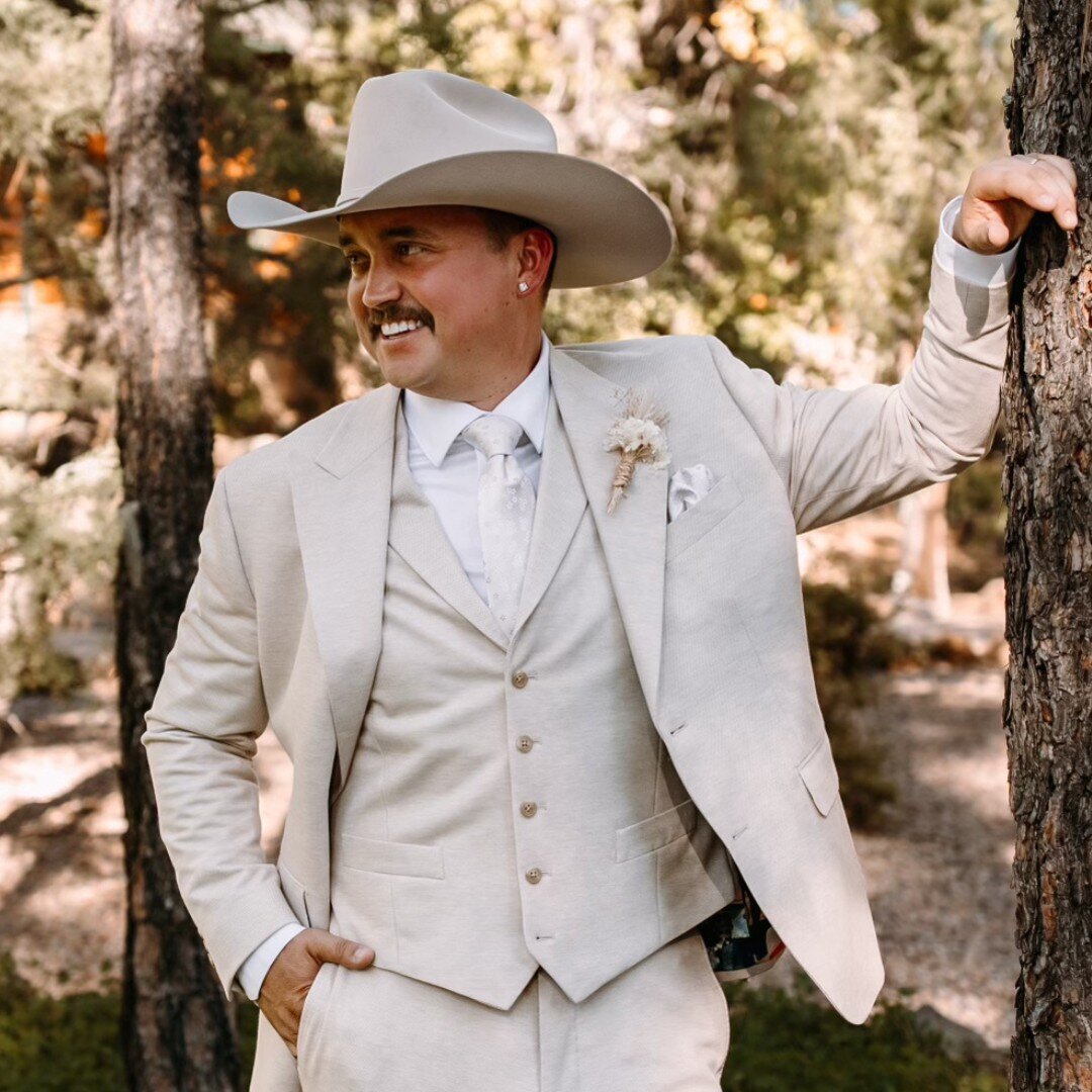A man in a wedding Western suit posing against a tree
