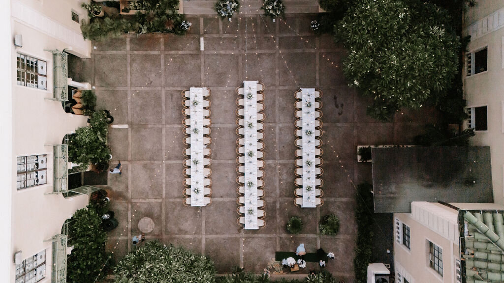 overhead view of three wedding reception tables that are very long and lined up with ivory tableclothes surrounded by buildings