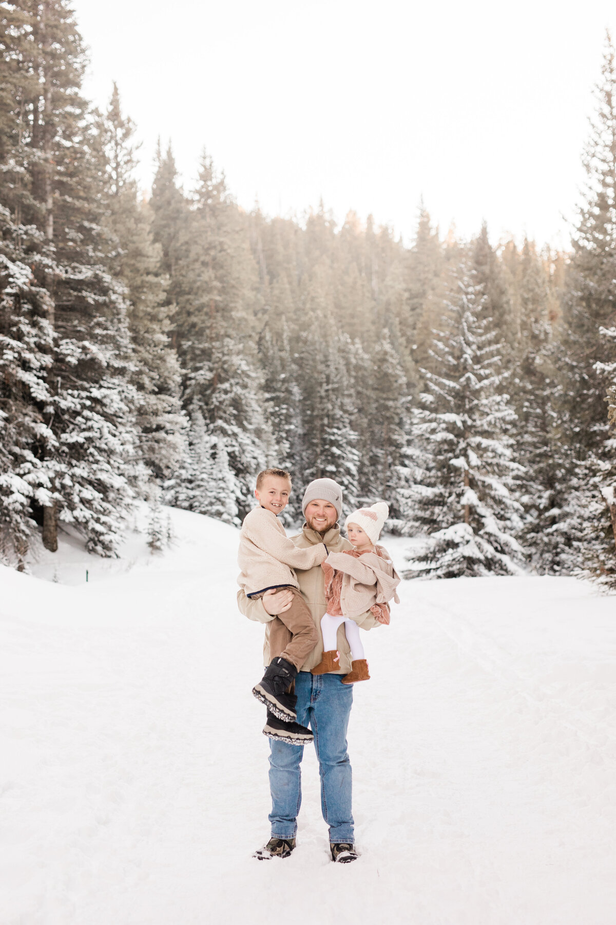 This dad hold two kids in his arms amidst a snowy winter landscape
