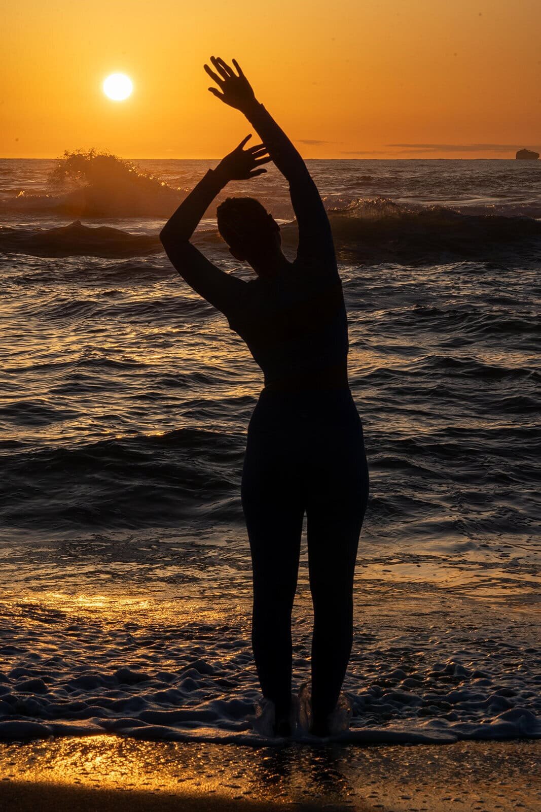 Woman in a yoga pose standing while watching the sun set over the ocean