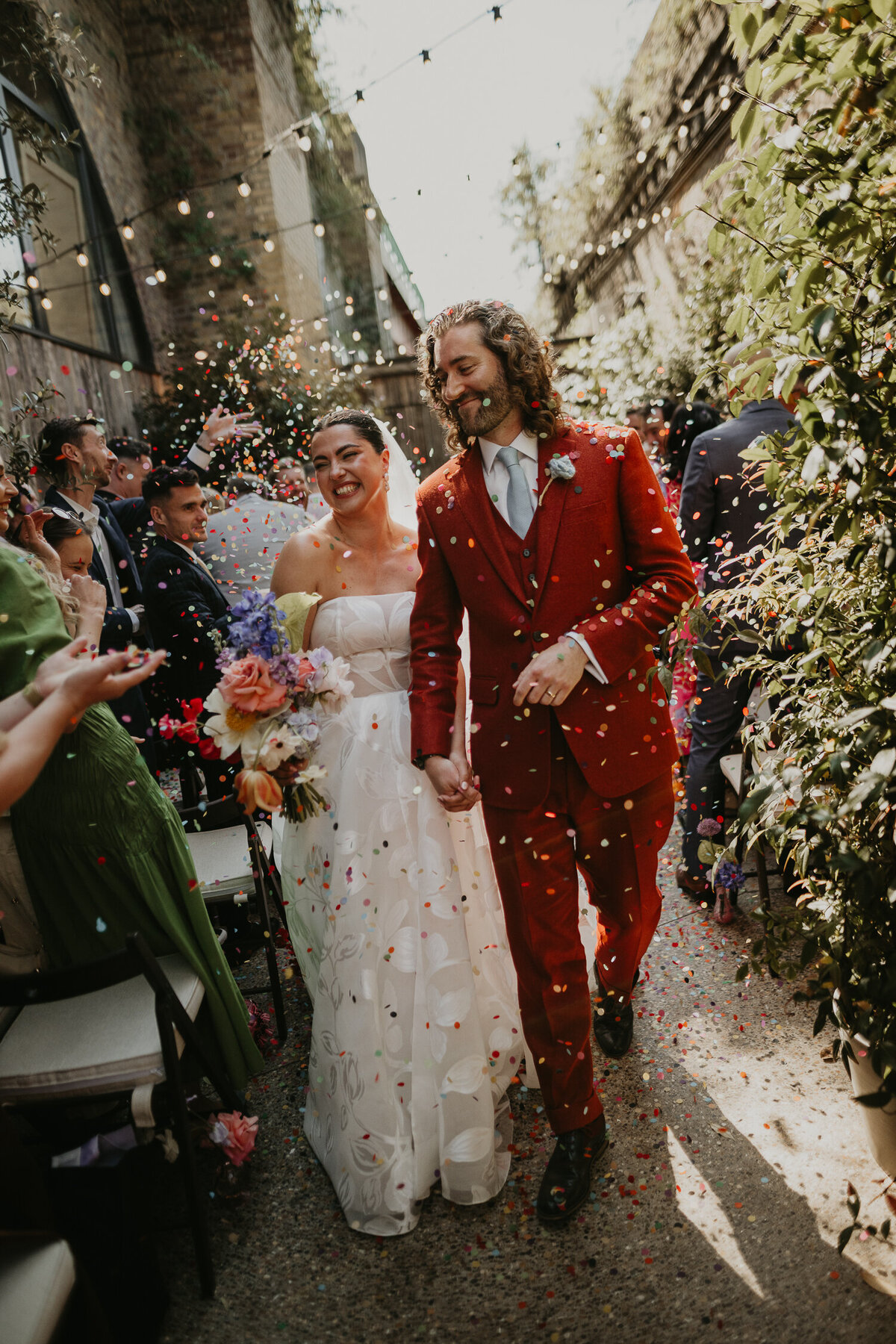 A bride and groom walk up the aisle as their wedding gusts throw confetti at 100 Barrington. 