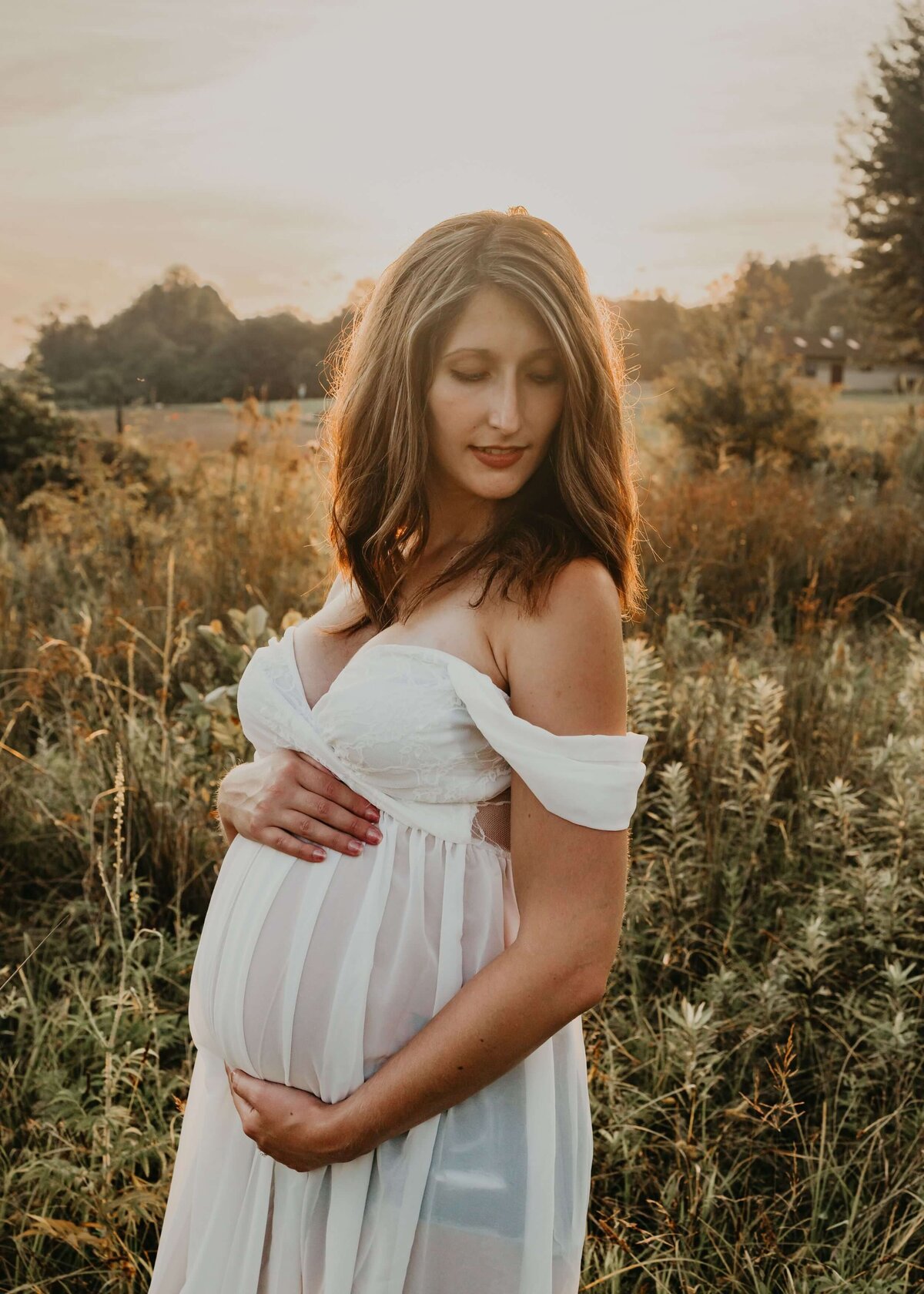 A pregnant woman in a white dress standing in a field, captured by a Pittsburgh maternity photographer.