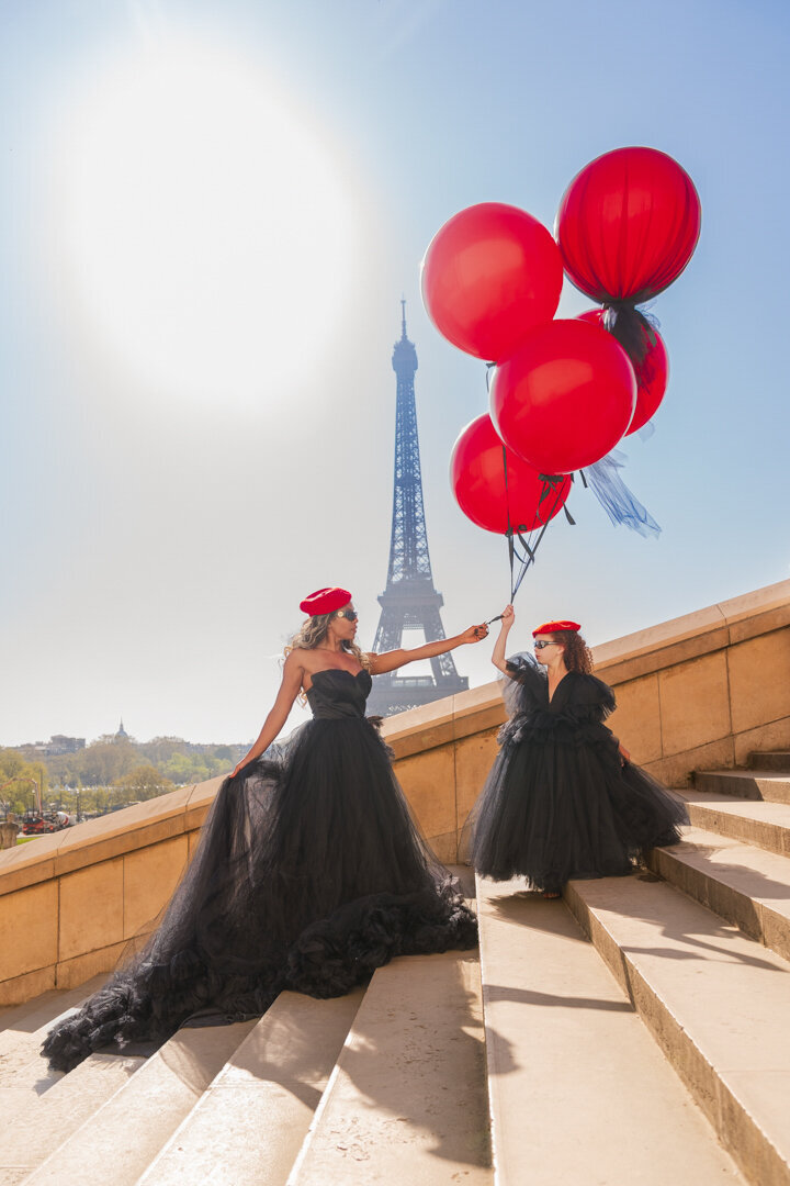 Iconic mommy and me Eiffel Tower shoot with chic black outfits, red accessories and bold balloons
