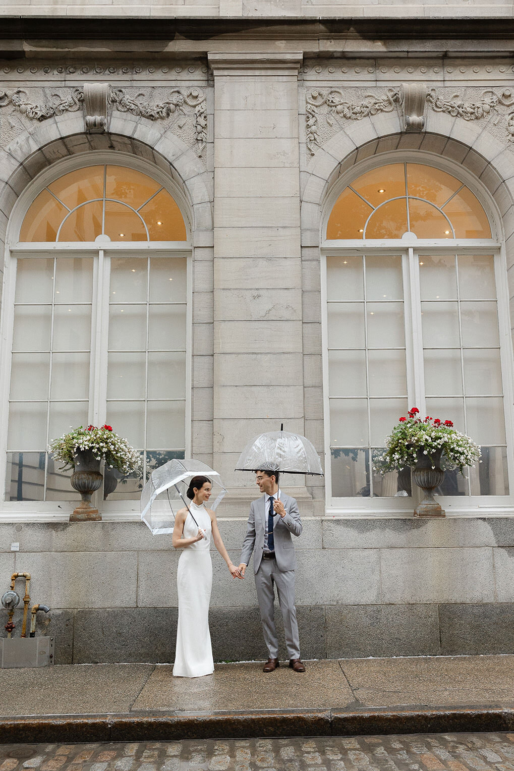 Couple de mariés avec deux parapluies transparent sous la pluie dans une petite rue de Montréal.