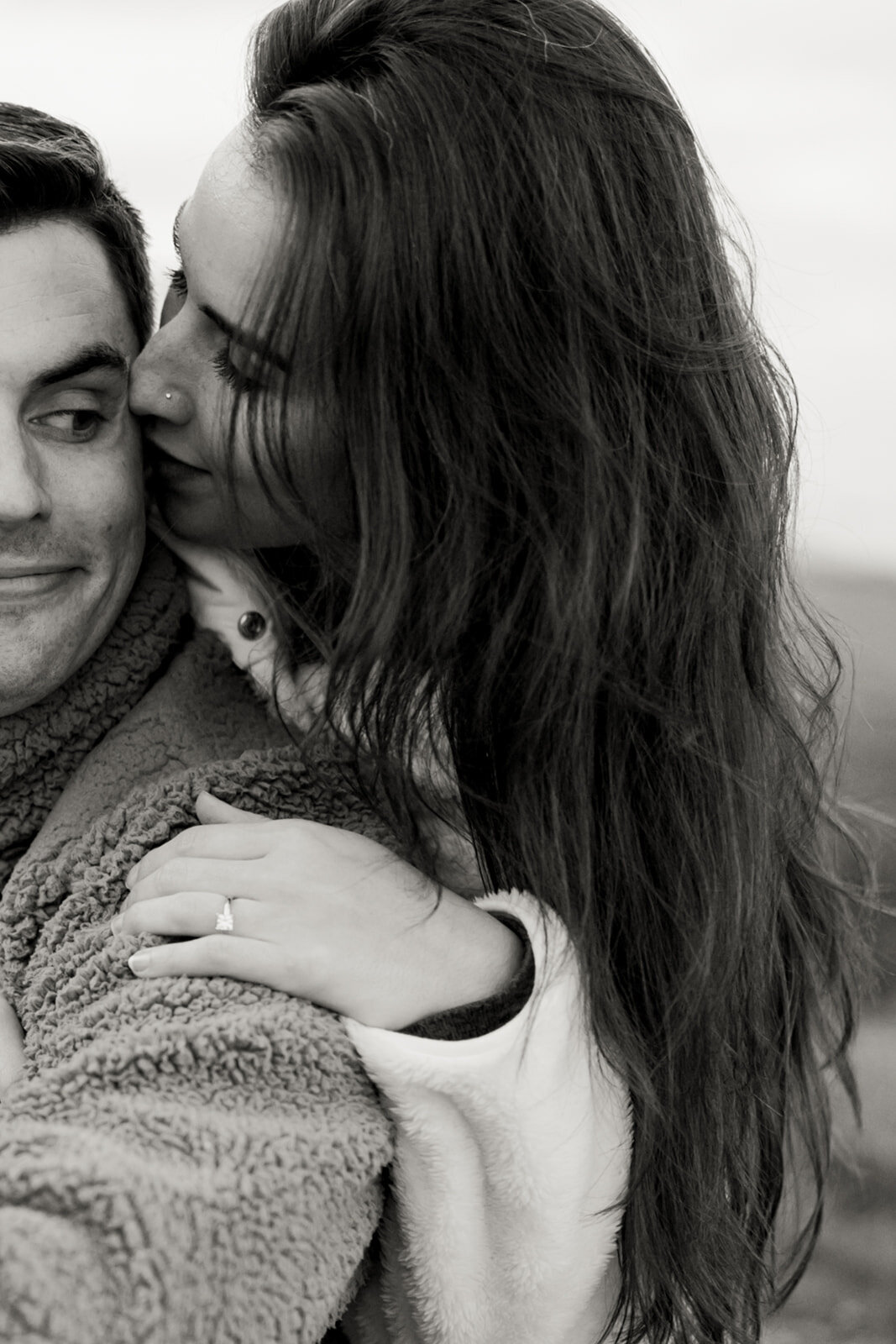 A candid black and white photo of a couple whispering and snuggling close in the chilly mountain air during their engagement session in Boone, North Carolina, captured by North Carolina wedding photographer Jessica Leigh Mason.

