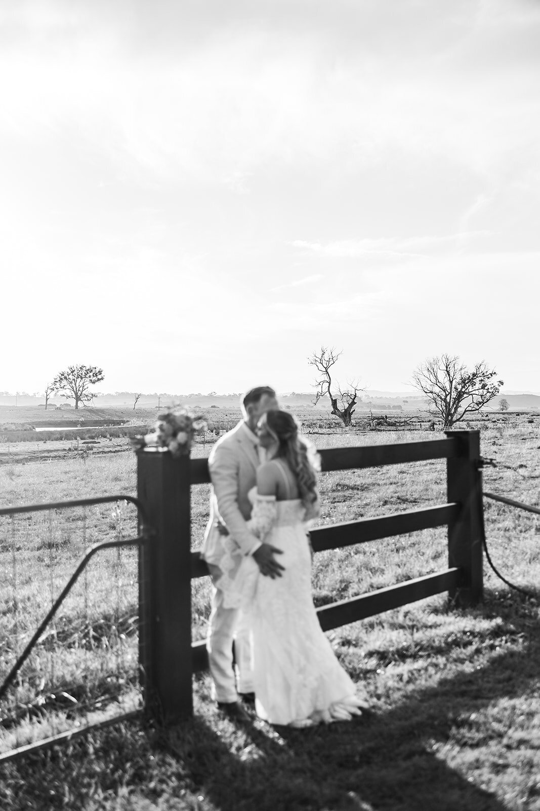 Blurred black and white image of a bride and groom hugging while leaning against a wooden fence at Petrichor Farm, a popular wedding venue near Canberra