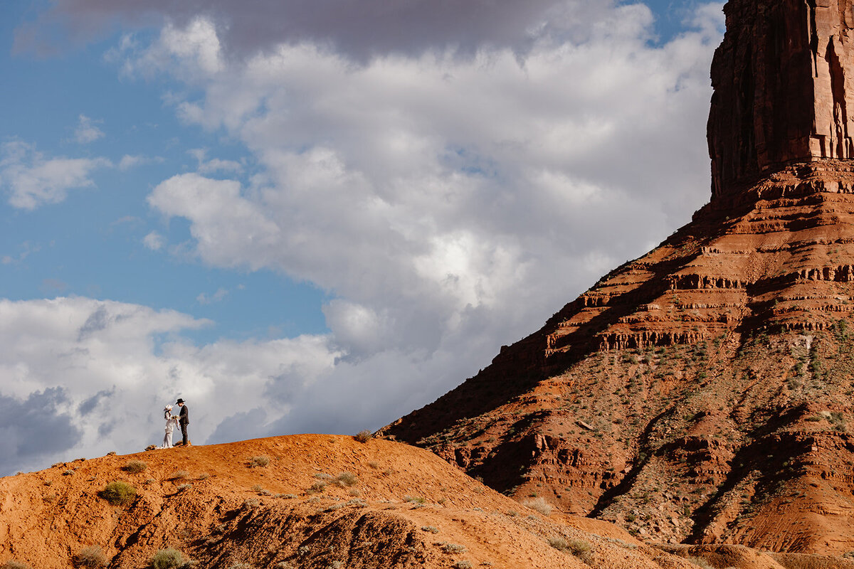 An eloping couple  at the top of a hill in Moab. They are facing each other, and holding hands. It is a shot that really focuses on the beauty of the scenery.