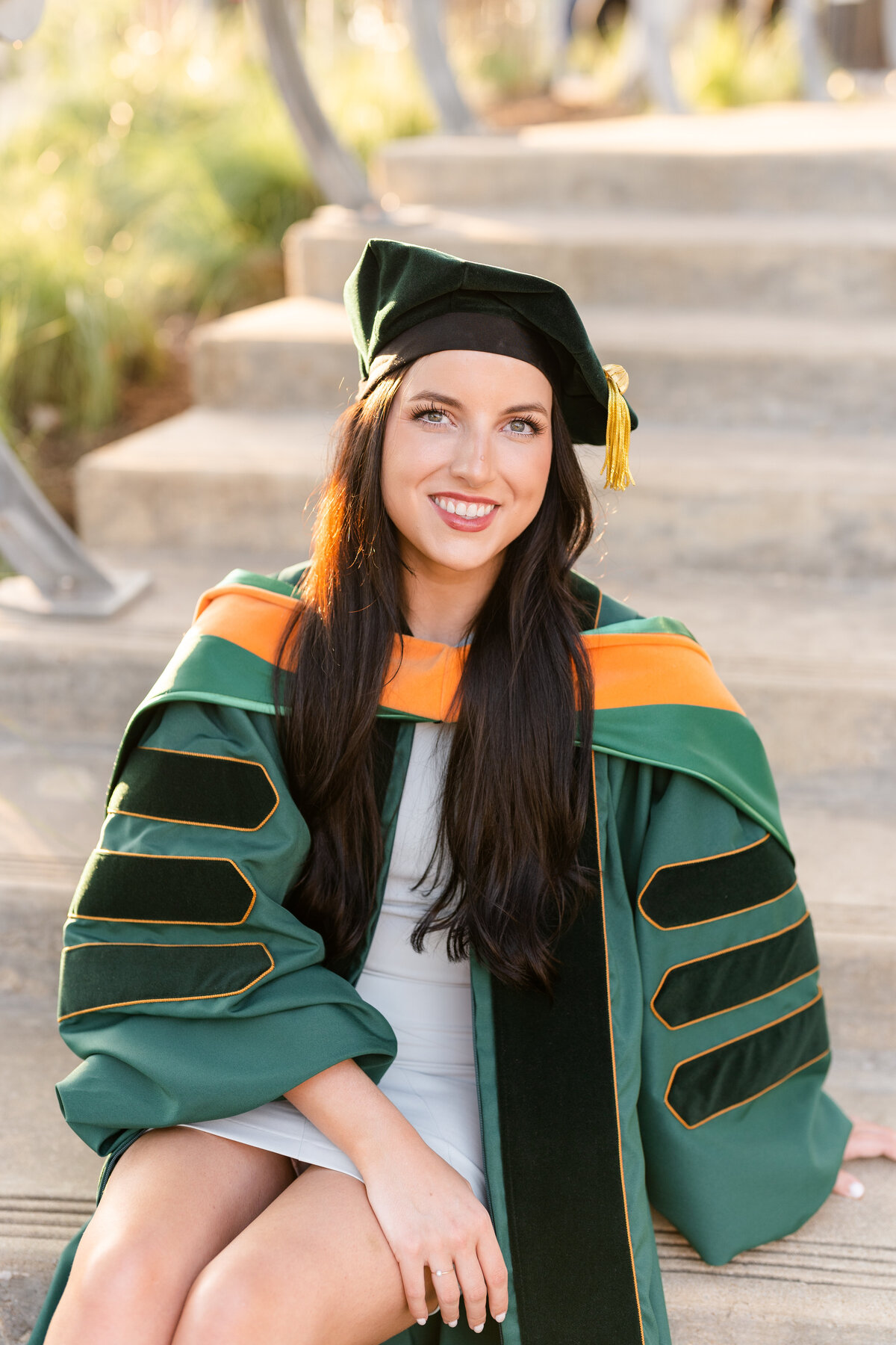 Baylor senior girl wearing doctorate gown, hood and hat while sitting on stairs and smiling in Downtown Houston