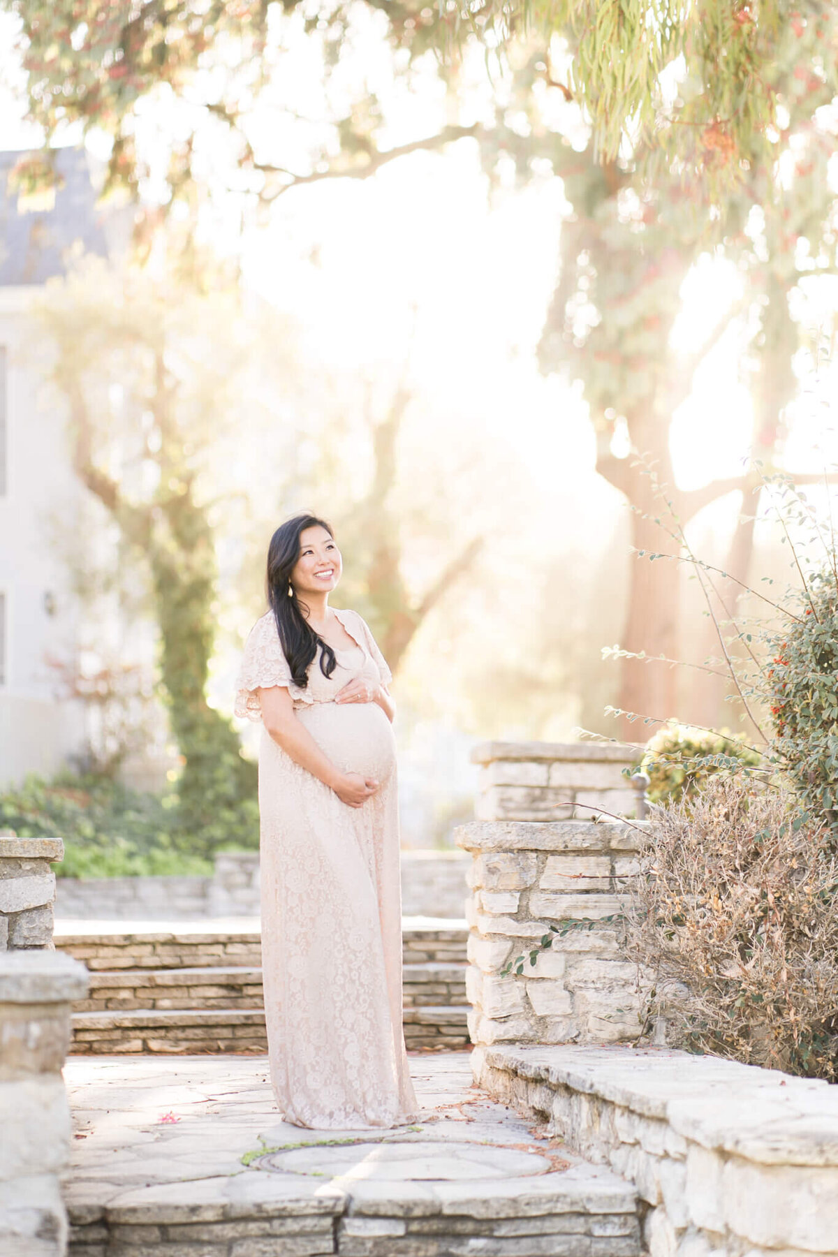 Pregnant mom holding maternity belly standing in brick pathway with glowing sun in the background.  By Orange County maternity photographer Melliemade Photography