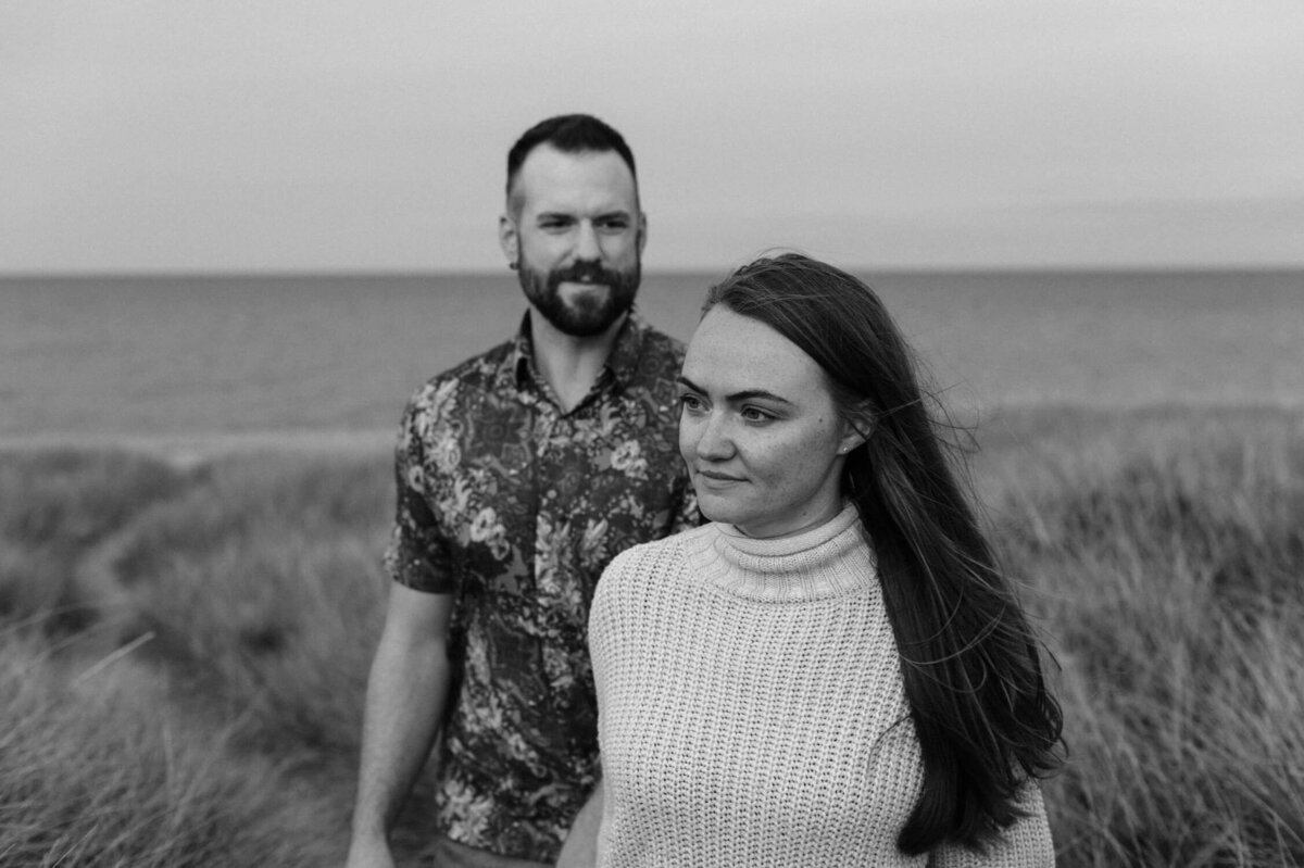 Moody couples portrait in front of grass and ocean.