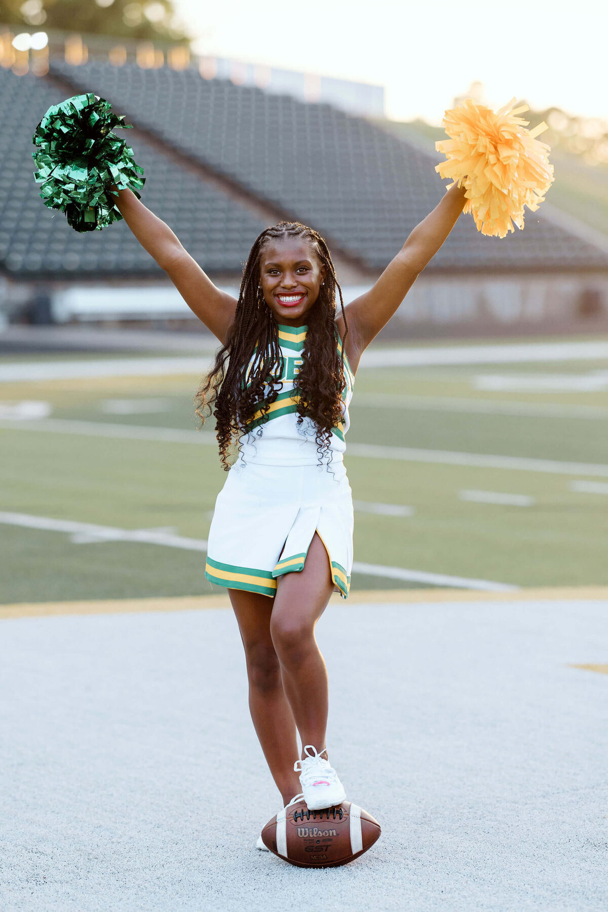 Longview Lobo senior cheerleader at Lobo stadium in white cheer uniform holding pom poms while standing on football