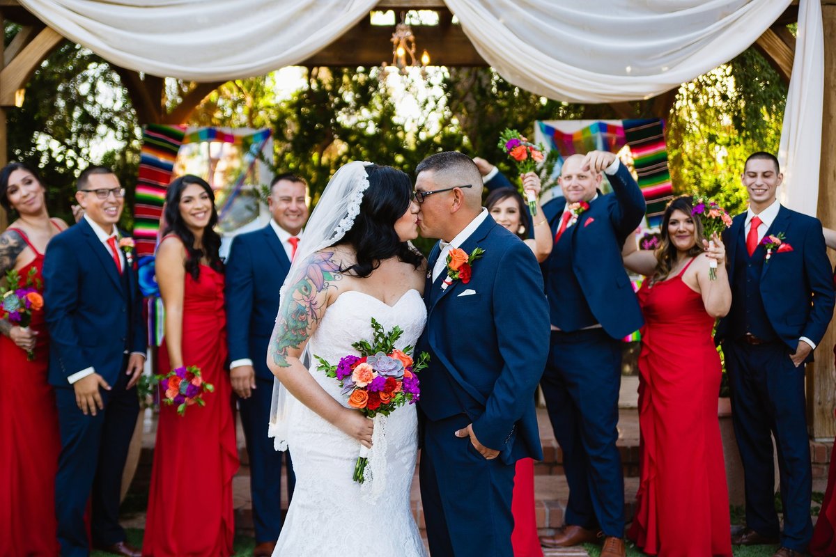Bride and groom kissing in front of their excited bridal party by PMA Photography.