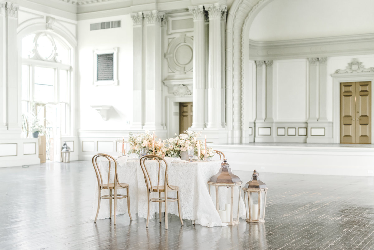 intimate wedding reception in a Bright and airy ballroom centered by a  table with peach and ivory flowers