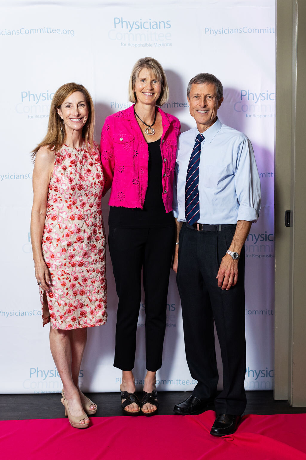 Three people pose on a red carpet.