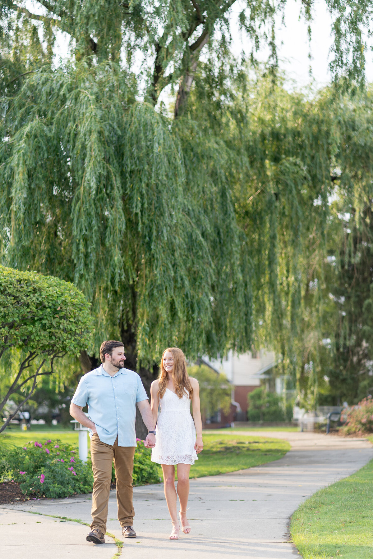 engaged couple walking down a stone path with willow trees in the background