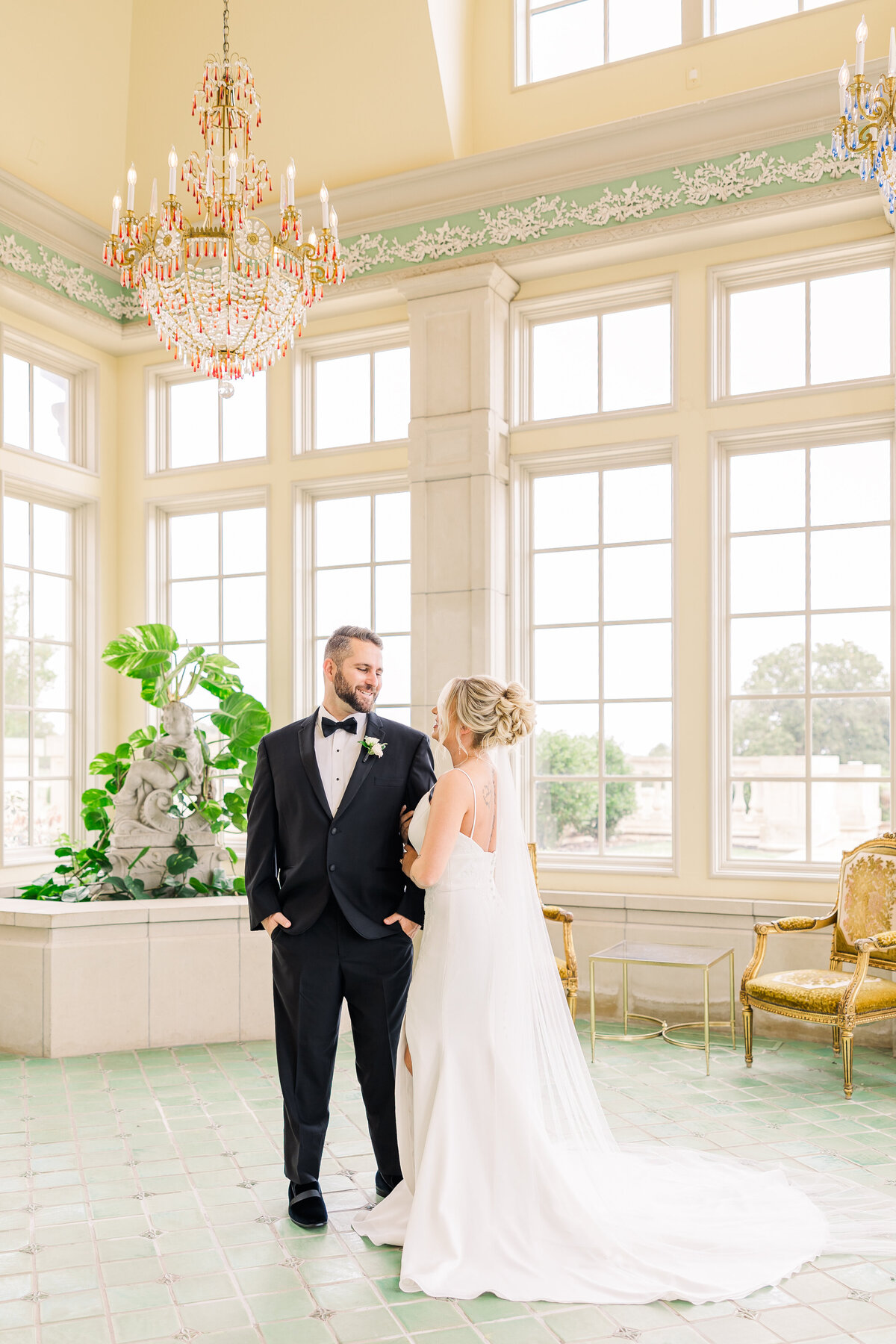 full-length-portrait-of-bride-and-groom-in-a-beauriful-room-with-chandelier-and-wall-of-windows
