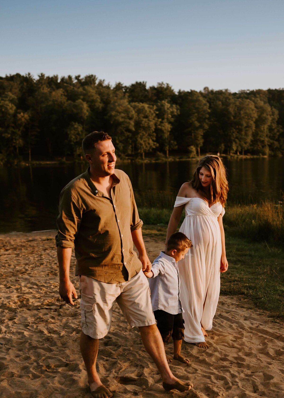 A family walks along the shore of a lake during their maternity session captured by a Pittsburgh maternity photographer.