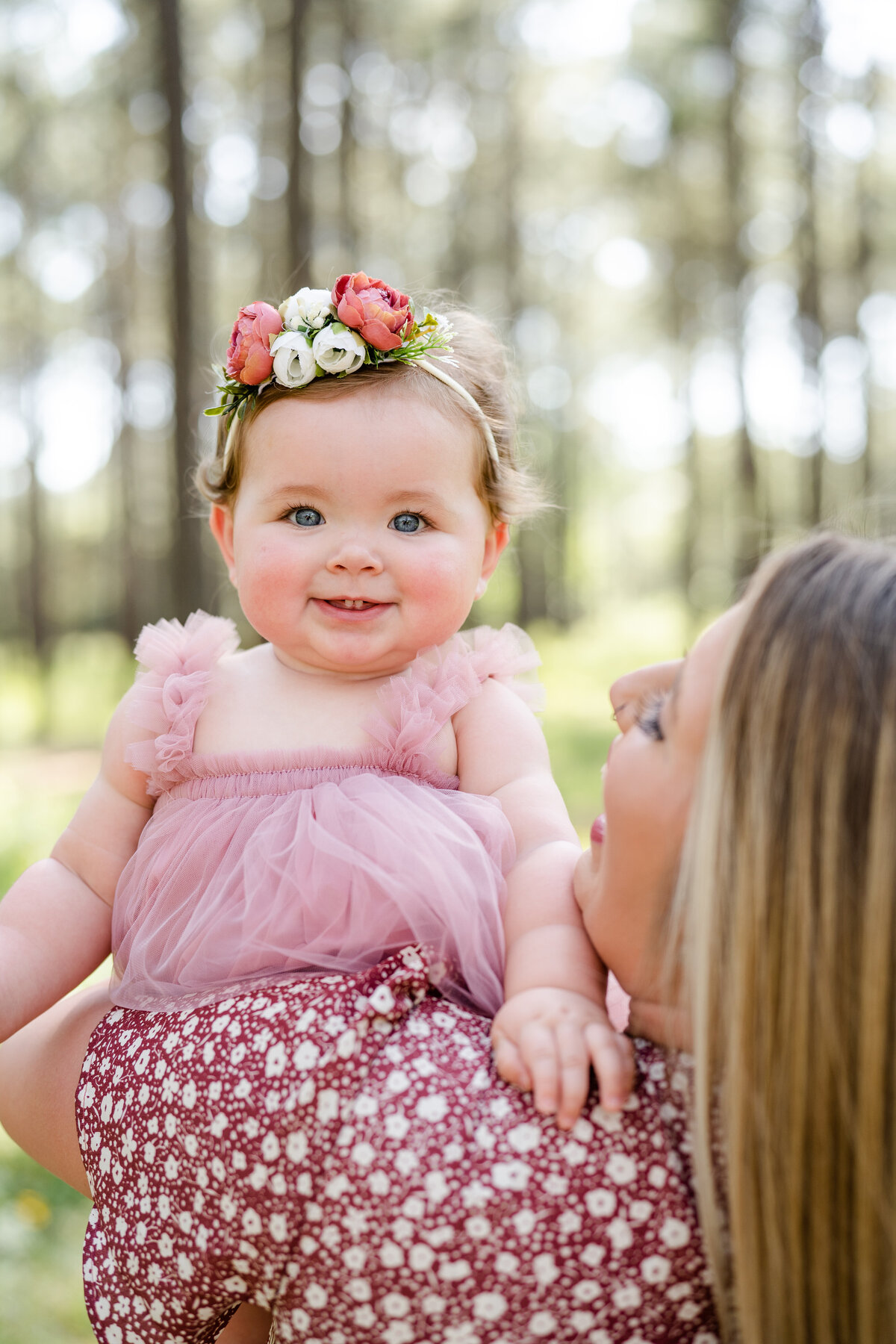 Little girl smiling over moms shoulder in a pink fluffy dress and flower headband at the W G Jones State Forest