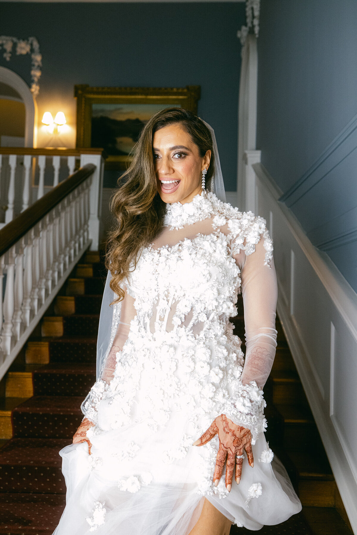 A wedding photo of the bride walking down a staircase in her white wedding dress