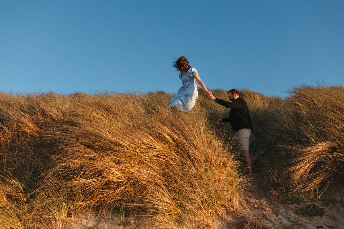 Photograph of a couple climbing the sand dunes at sunset in West Cornwall