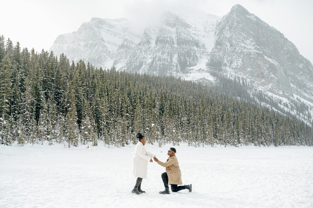 Couple stands in the middle of a snowy clearing at Lake Louise during a magical winter proposal.