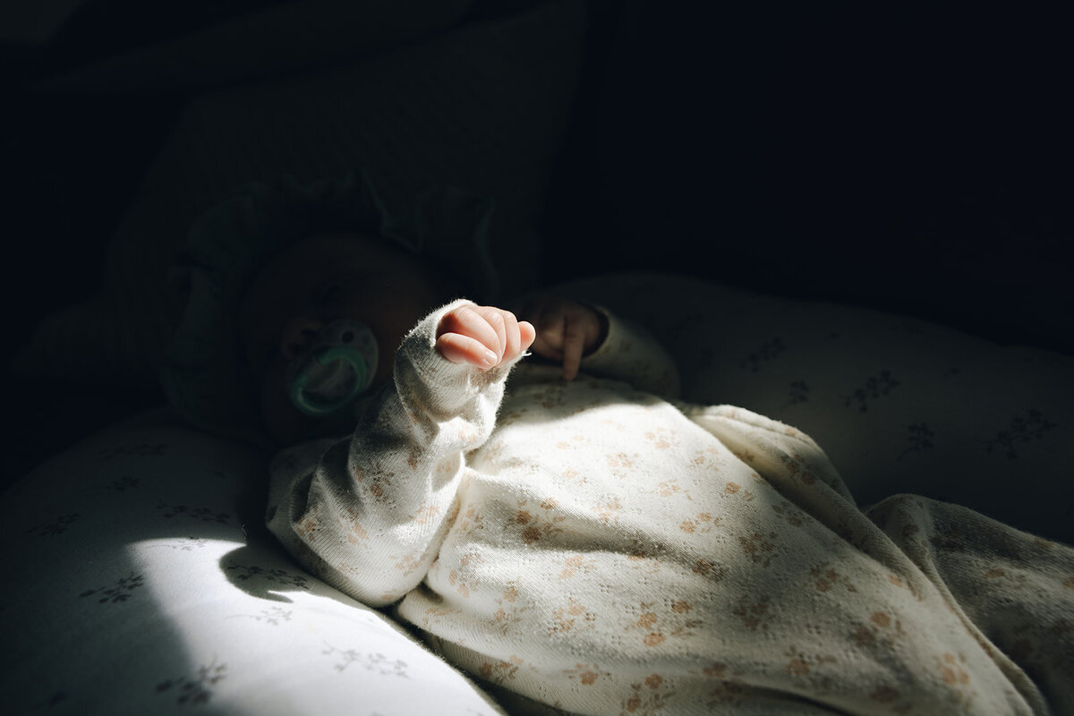 Newborn hand relaxes in the sunlight while baby lays napping. 