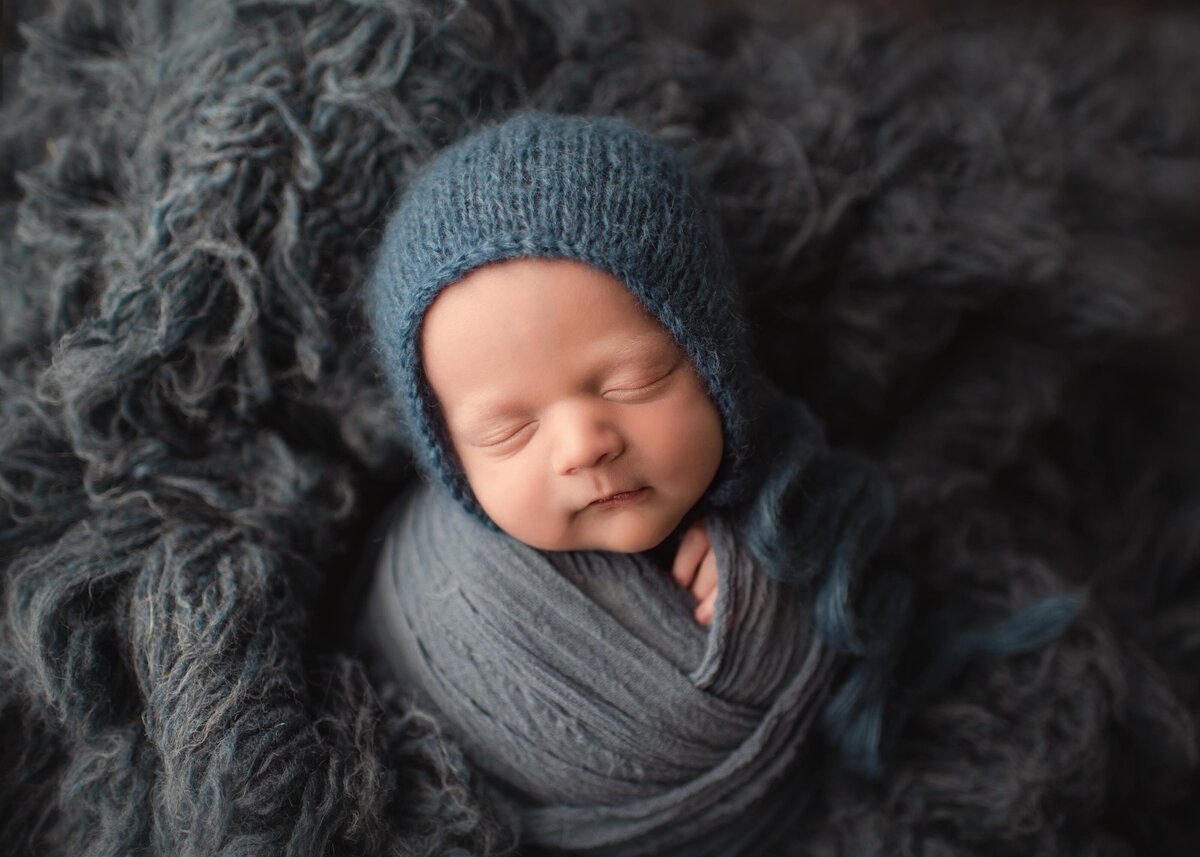 Sleeping baby in blue bonnet and wrap on blue flokati