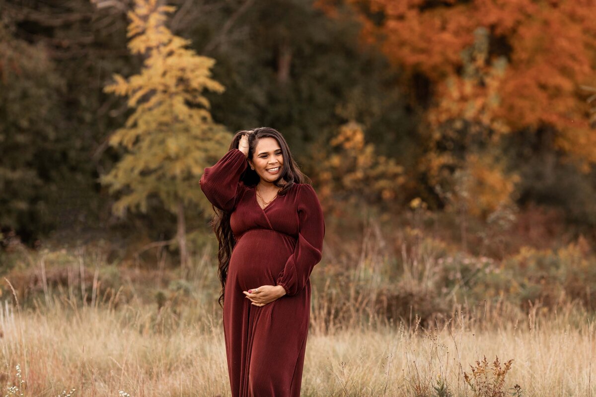 london ontario fall maternity photos mom smiling with  vibrant orange tree