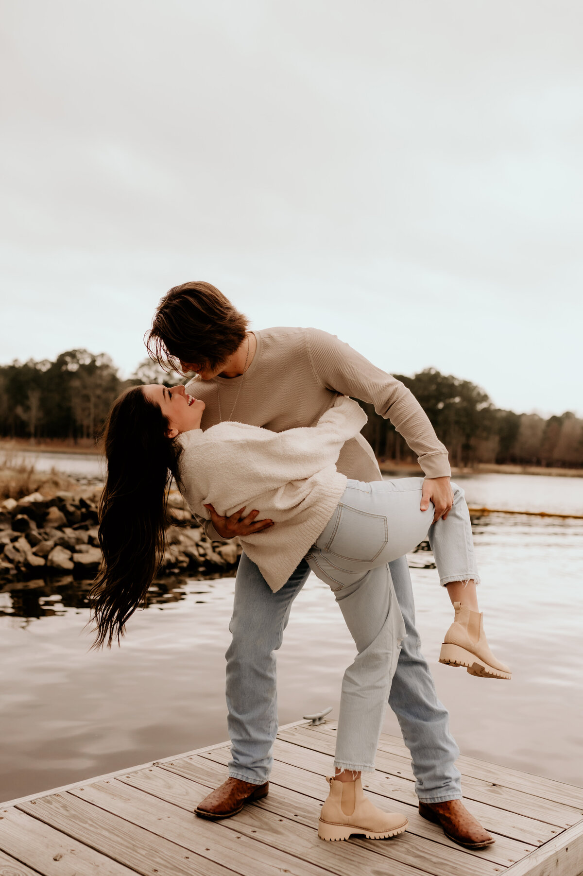 man and woman on a pier on a lake dancing as the man dips the woman back and they laugh together photographed by Little rock engagement photographer