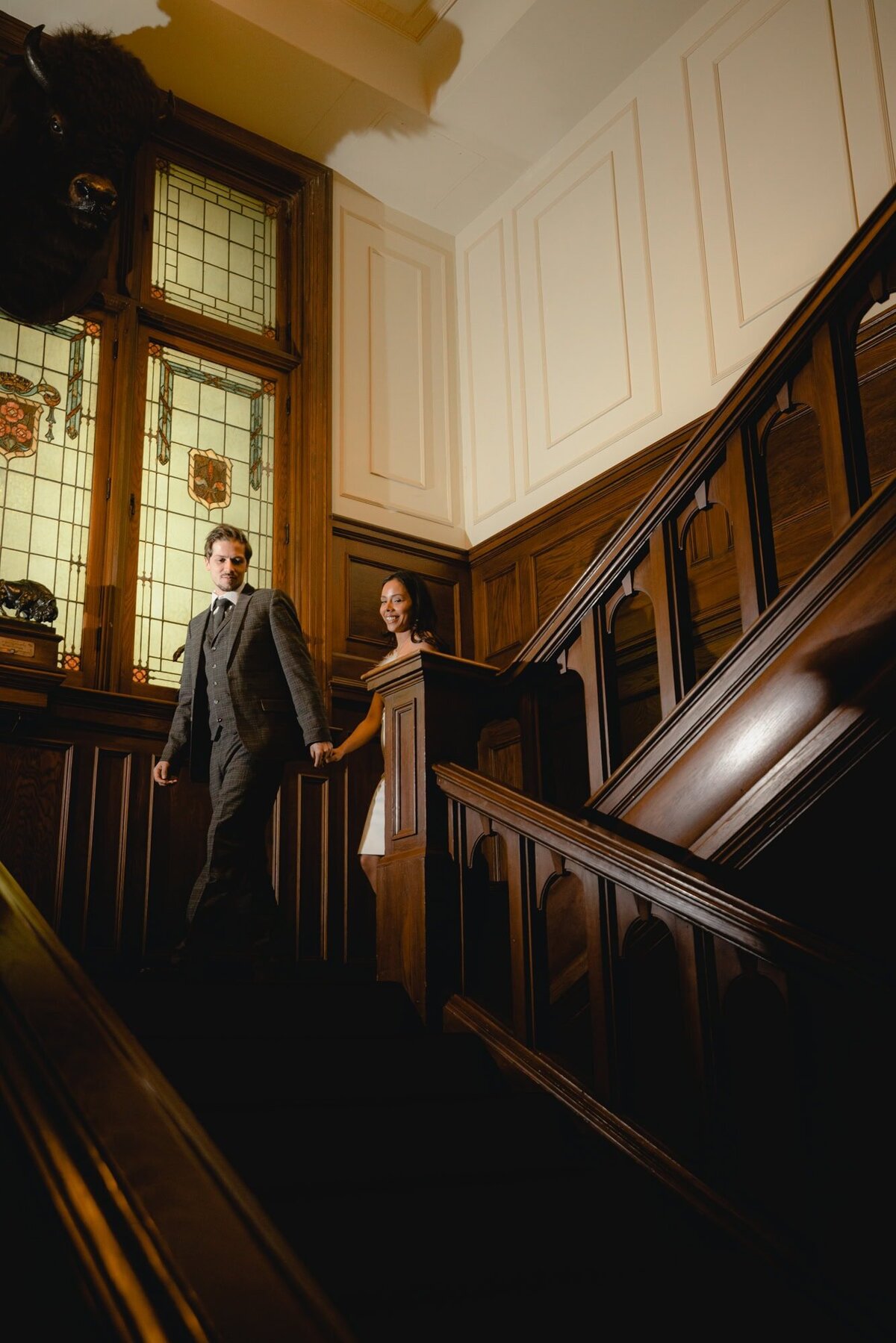 Wedding couple walk down stairs in historic The Ranchmen's Club in Calgary