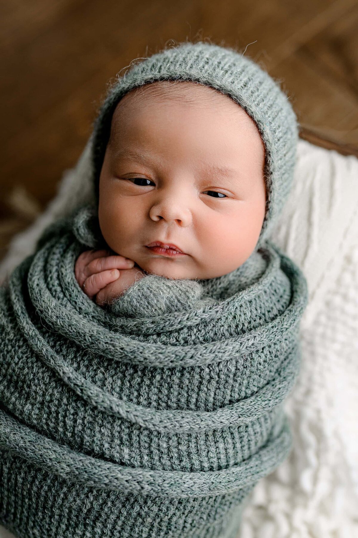 close up image of a newborn baby boy wrapped in green wearing a hat