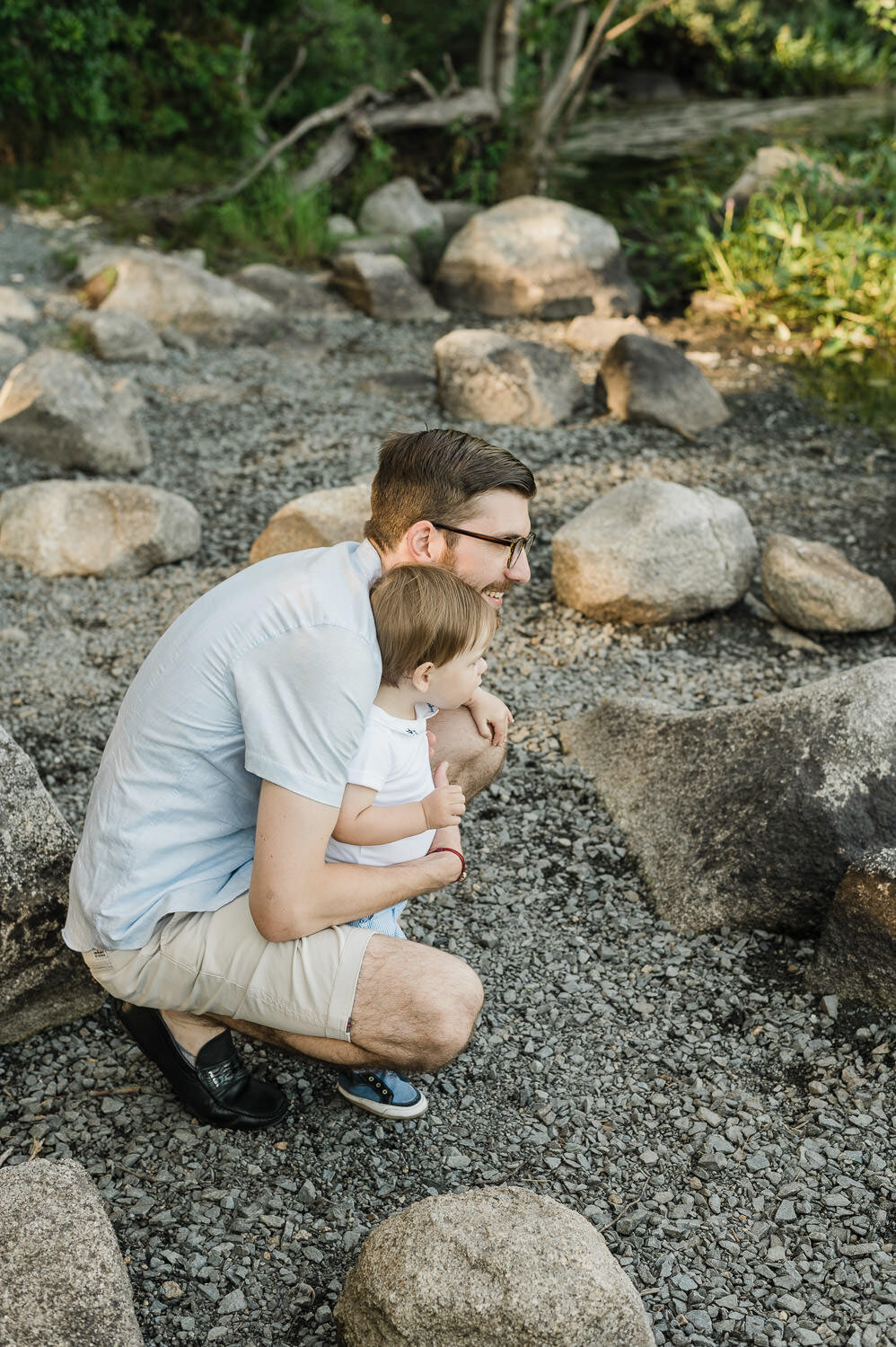 Parent crouching with toddler on rocks.