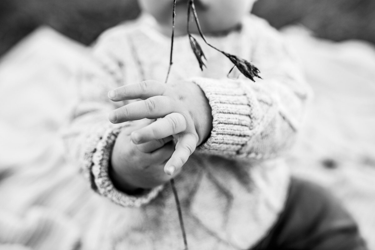 A black and white image of a baby holding a blade of grass.