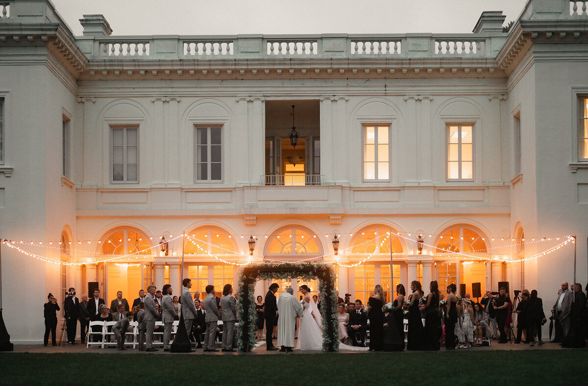 wedding ceremony photograph showing bride and groom and all of their guests with the wadsworth mansion wedding venue in background photo by cait fletcher photography