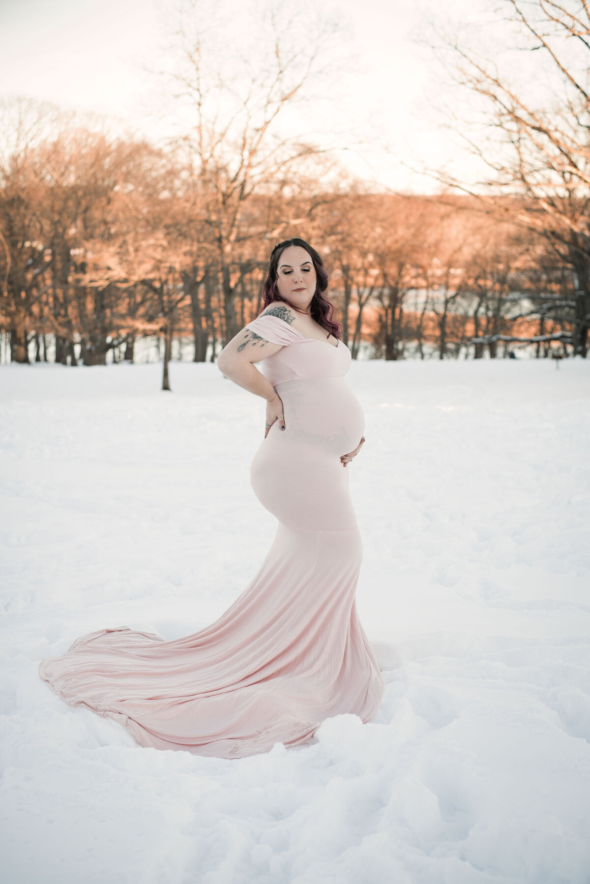 35 week pregnant lady wearing white fitted maternity gown holding baby bump standing in the snow