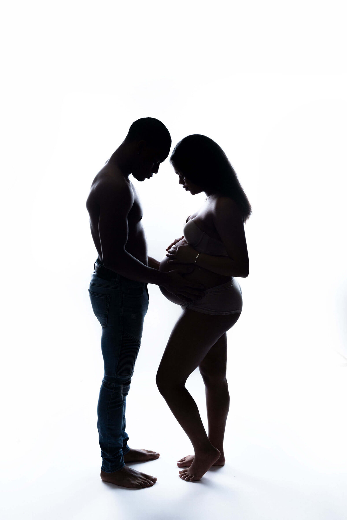 Silhouette of a pregnant woman standing in a studio with her husband in underwear with hands on her bump taken by a New Orleans Maternity Photographer