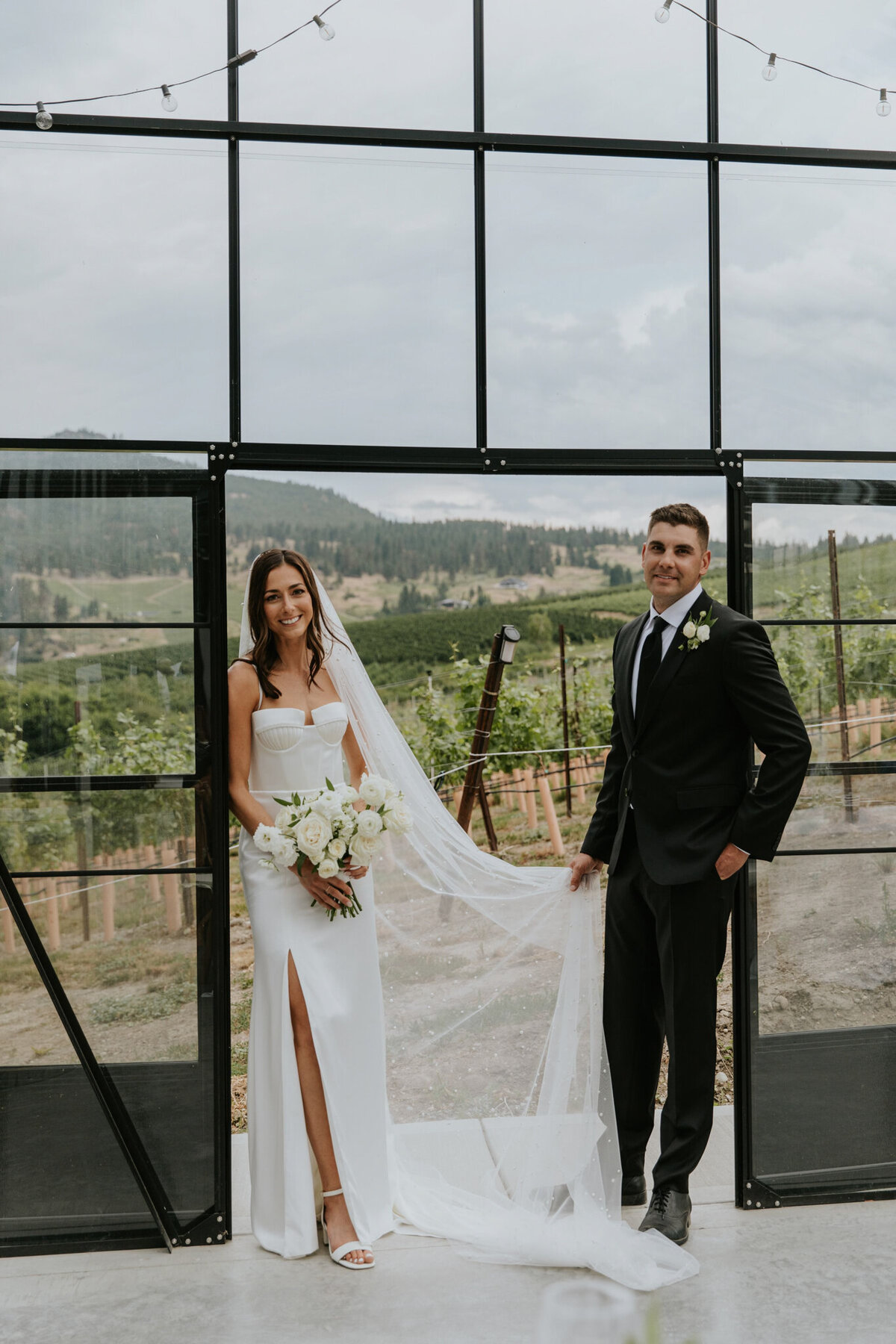 Bride and groom in doorway of 99 Rows, white rose bouquet by Valley Bloom Co, bright and airy wedding florals based in Kelowna, BC. Featured on the Brontë Bride Vendor Guide.