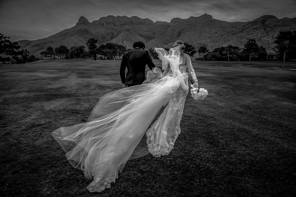 A couple walk together toward the Franklin Mountains at Coronado Country Club in El Paso as her dress blows in the wind