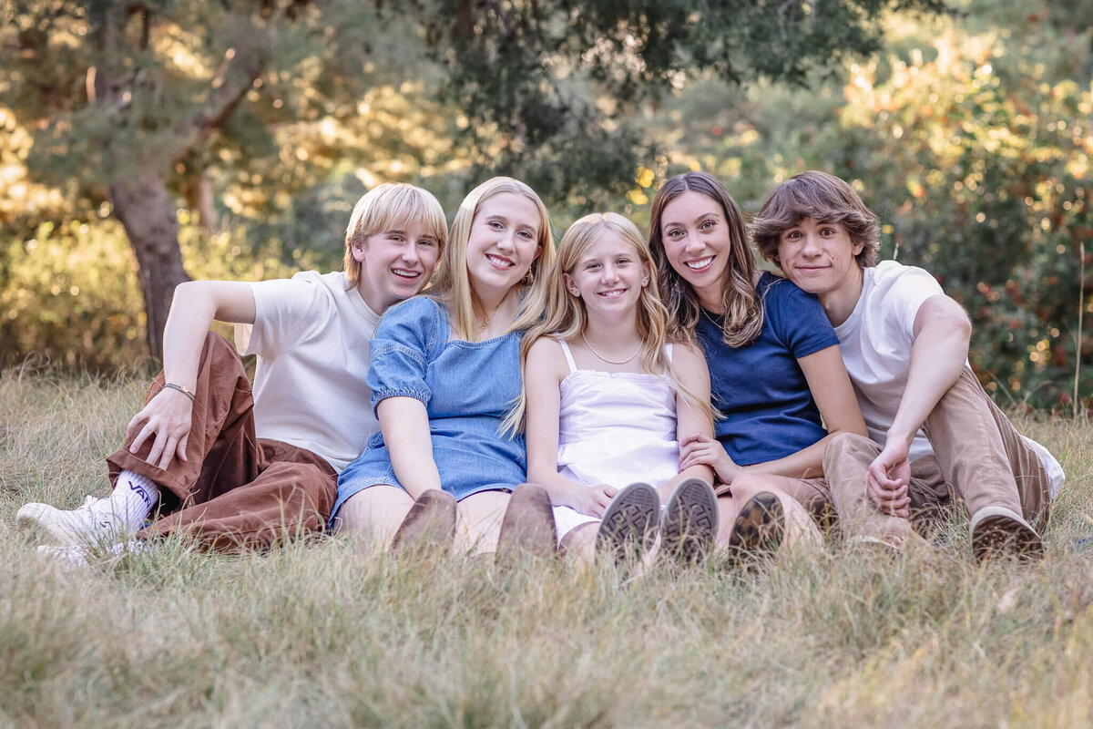 Five cousins sitting in the grass, smiling at the camera and wearing shades of blue and white at Jeffrey Open Space.