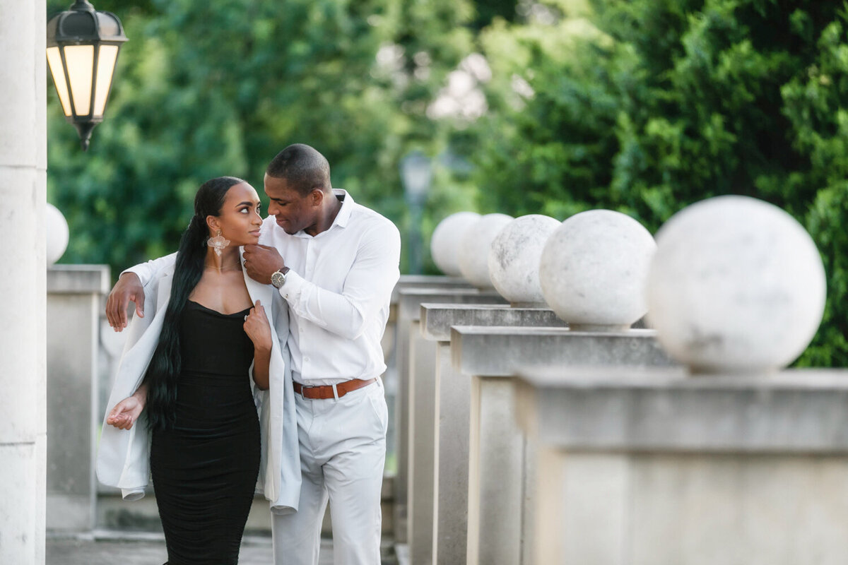 Couple at Adriatica Village in Dallas during their engagement session, he covers her with his jacket and gently touches her chin to bring her in for a kiss.