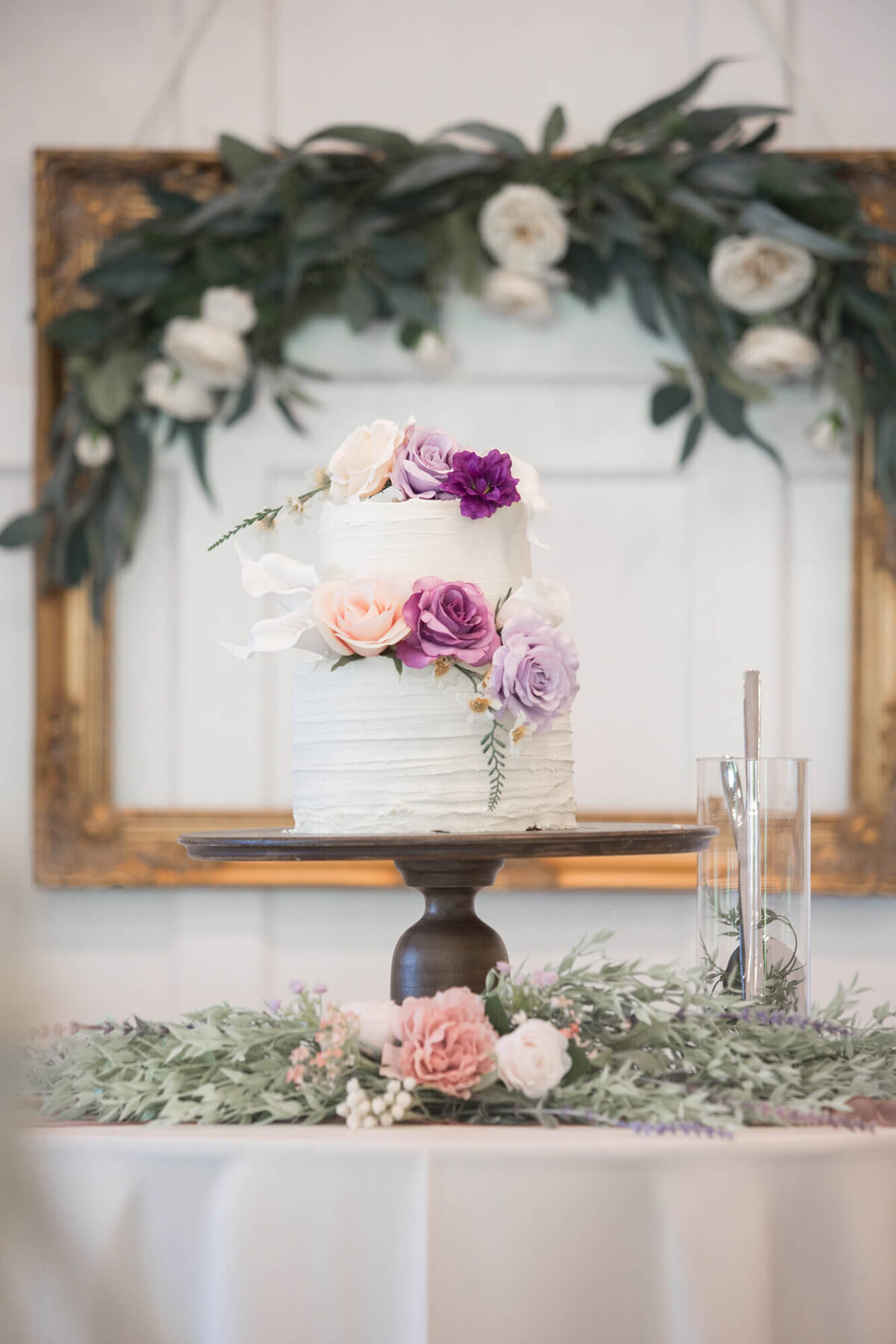 a two tier wedding cake with white, pink, and purple roses