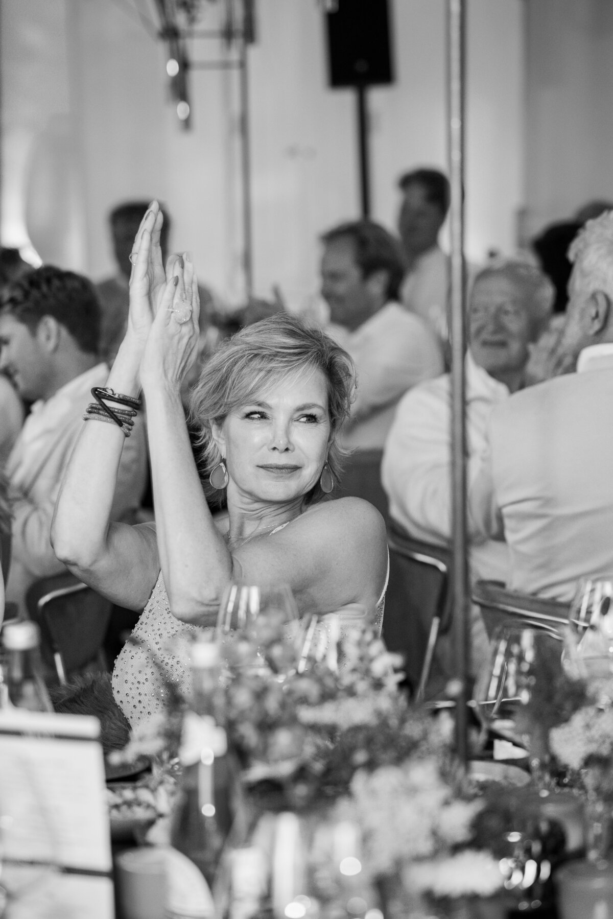 A woman enthusiastically claps during a performance at a luxury event. The black-and-white image captures her joyful reaction and the vibrant atmosphere of the evening.